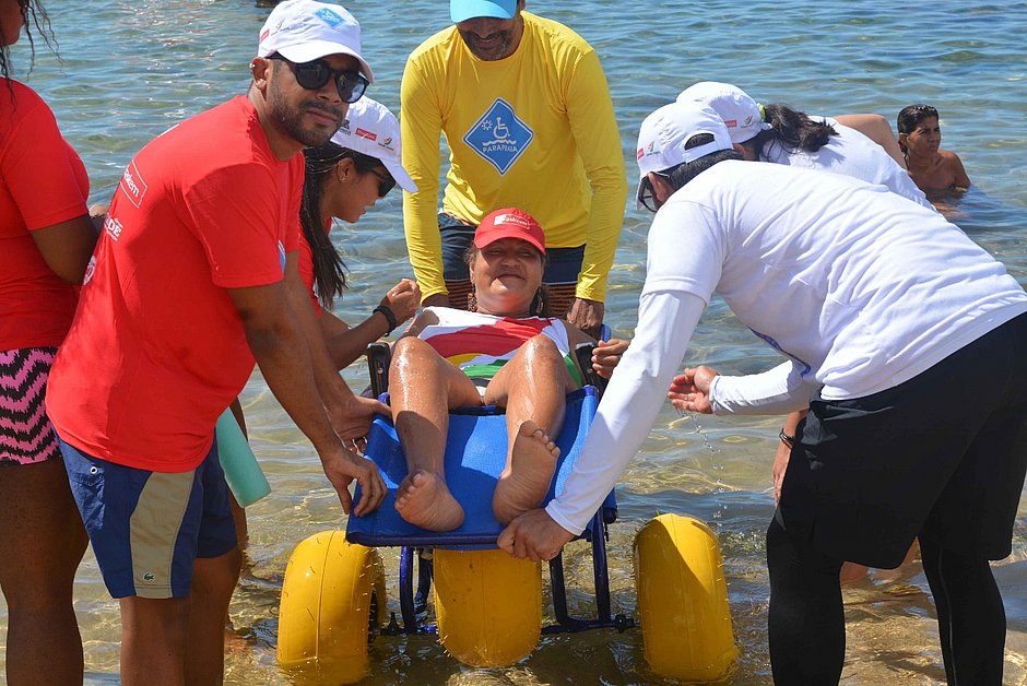 Cadeirante entrando no mar com ajuda de voluntários
