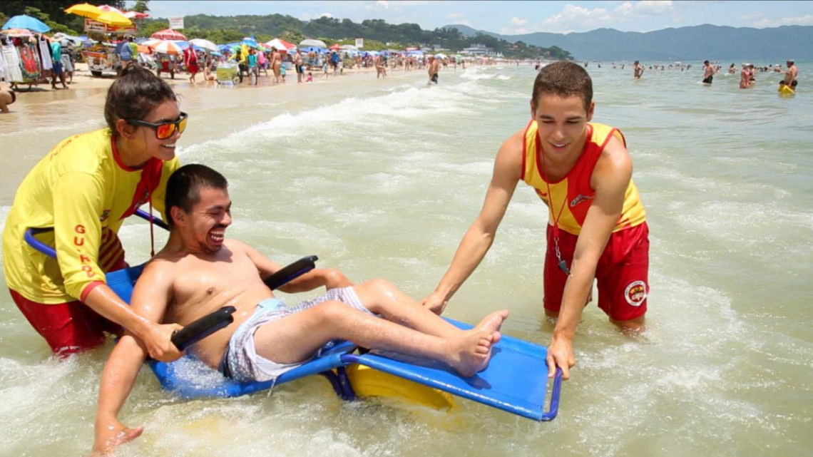 Cadeirante dentro do mar com 2 salva vidas ao lado