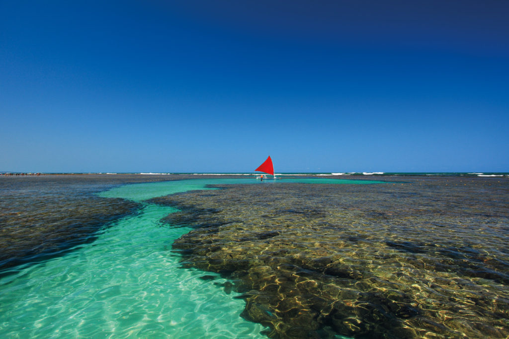 Recife com uma jangada ao fundo