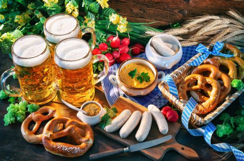Vários quitutes da culinária alemã, como salsicha branca, pretzel, mostarda, cerveja sobre a mesa rústica