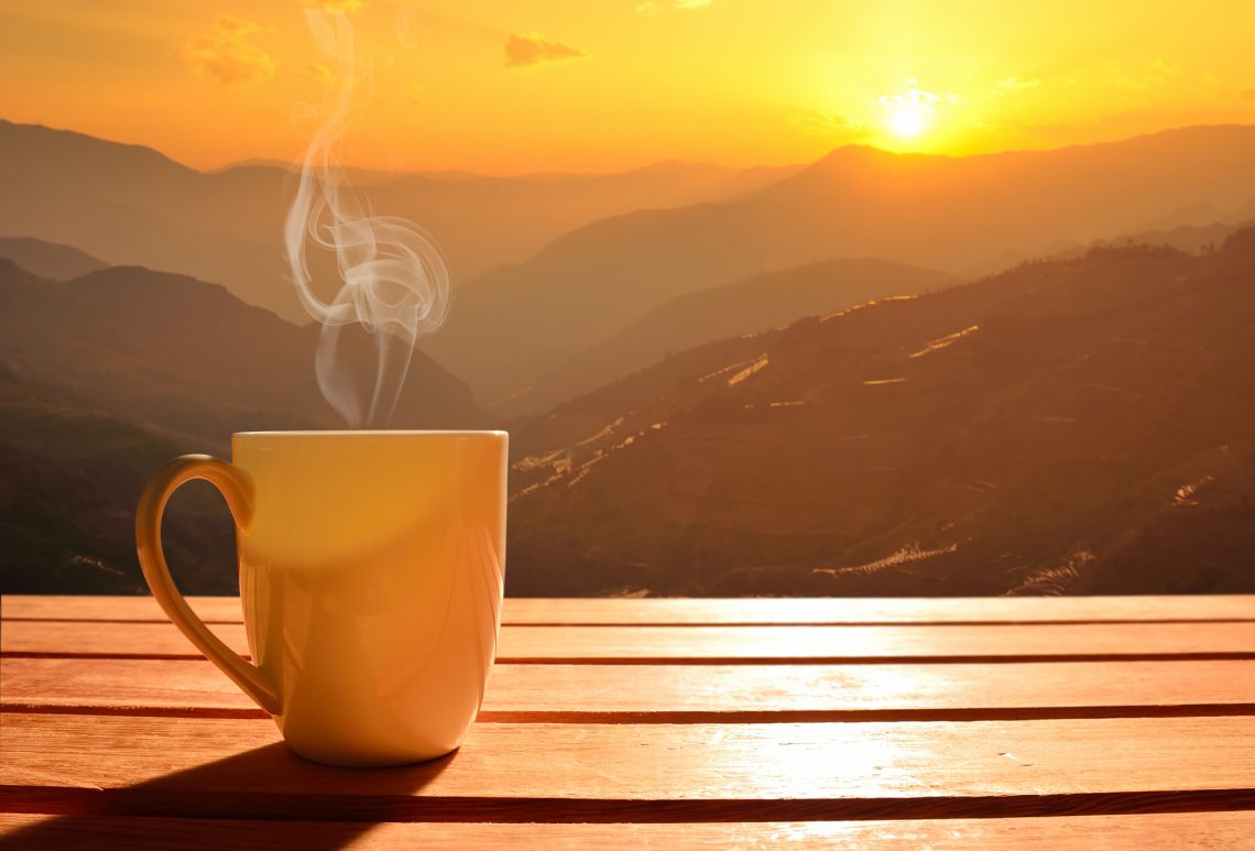 Xícara do café e o nascer do sol ao fundo