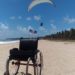 cadeira de rodas na praia e ao fundo o parapente